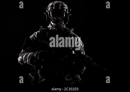 Army special operations forces soldier in mask and combat uniform, armed submachine gun, low key studio portrait on black, copyspace contour shot Stock Photo