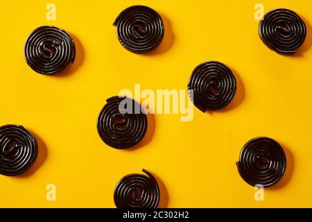 Spiral coils of fresh liquorice candy scattered on a colorful vibrant yellow background in a full frame view Stock Photo