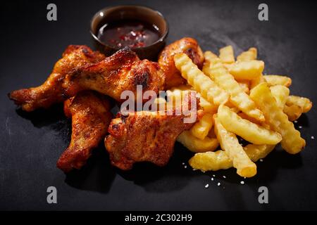 Close up on crispy spicy grilled chicken wings with chili dip on the side and a serving of oven baked crinkle cut potato chips for menu advertising Stock Photo
