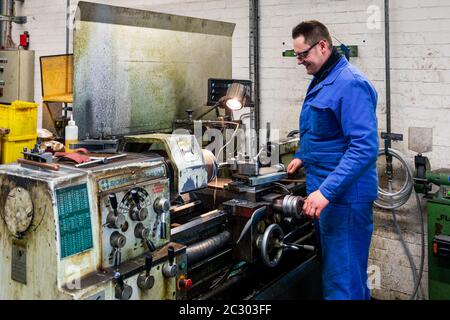 A worker in blue overall is working at a lathe machine Stock Photo