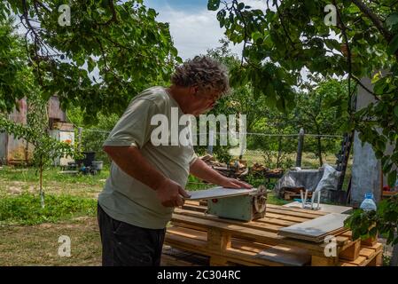 Caucasian Senior Man using circular saw for cutting parquet plank in the garden Stock Photo