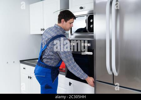Male Technician In Overall Installing Oven In Kitchen Stock Photo