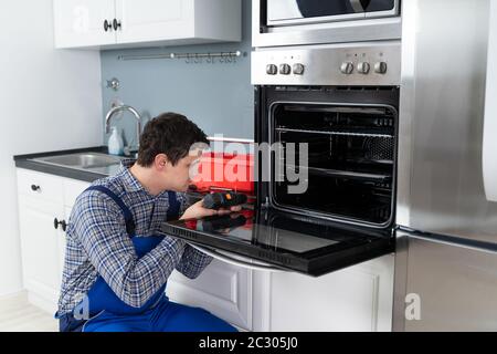 Male Technician In Overall Installing Oven In Kitchen Stock Photo
