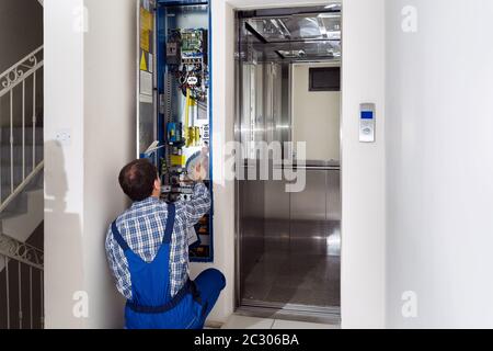 Technician Repairing Control Panel Of Broken Elevator Stock Photo