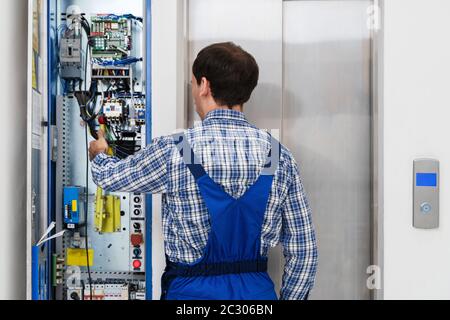 Technician Repairing Control Panel Of Broken Elevator Stock Photo