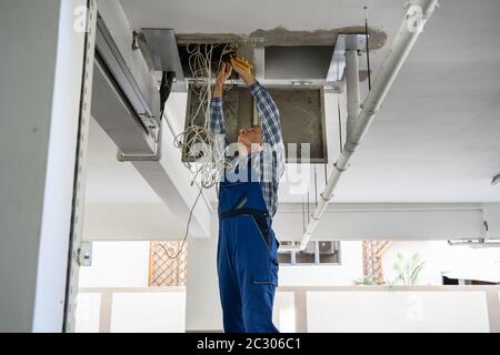 Male Electrician On Step Ladder Installing Light At Corridor Stock Photo