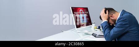 Worried Businessman Near Computer With Ransomware Word On The Screen At The Workplace Stock Photo