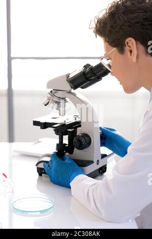 Over shoulder view of concentrated lab researcher using microscope while working with medical sample in laboratory Stock Photo