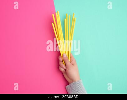 hand holds a stack of yellow paper tubes for a cocktail on a multi-colored background, concept of rejection of plastic and the use of recyclable mater Stock Photo