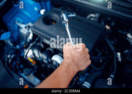 Worker in uniform disassembles vehicle engine, car service station. Automobile checking and inspection, professional diagnostics and repair Stock Photo