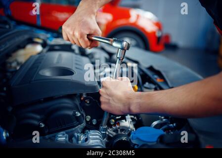 Worker in uniform disassembles vehicle engine, car service station. Automobile checking and inspection, professional diagnostics and repair Stock Photo