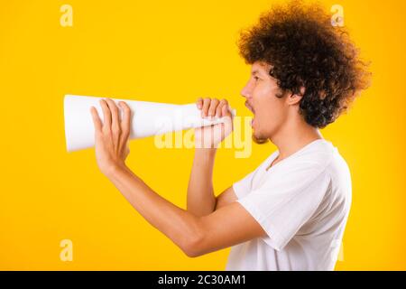 Asian handsome man with curly hair he announcing or spreading news using white speaker paper isolate on yellow background Stock Photo