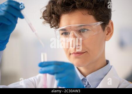 Close-up of focused chemist in protective goggles dropping reagent while examining chemical reaction Stock Photo