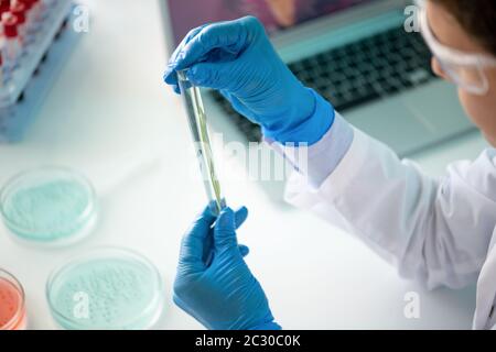 Close-up of biologist sitting at desk with petri dishes and mixing samples in test tube Stock Photo