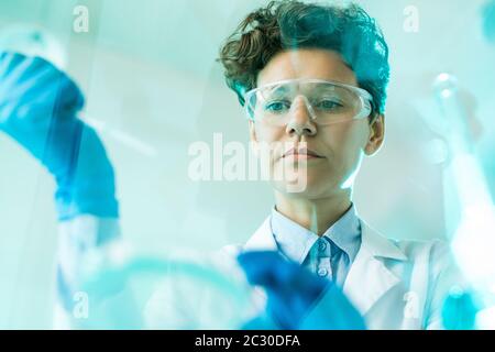 Below view of concentrated female research scientist in safety goggles working with samples in laboratory Stock Photo