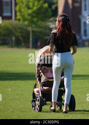 Attractive woman pushing a stroller in the park with defocused background Stock Photo