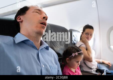 Annoyed Woman Looking At Her Husband Snoring Loud While Sleeping In Airplane Stock Photo