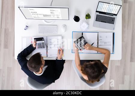 Two Young Businesspeople Calculating Invoice With Calculator Stock Photo