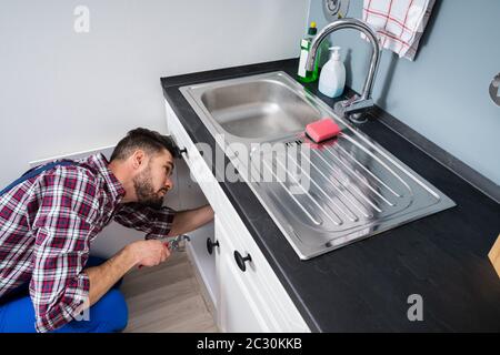 Male Plumber In Overall Fixing Sink Pipe Stock Photo