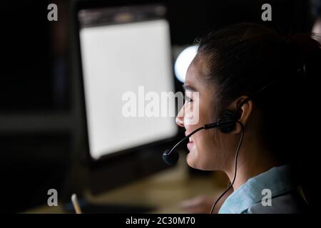 Late Night Environment. Side view young adult friendly Call centre operator with headsets working hard at night. Using for 24 Hr. 7 days Call center C Stock Photo
