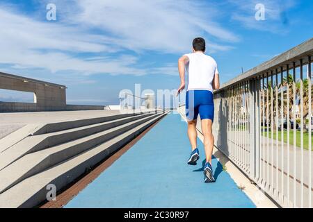 Young runner man in blue pants and white t-shirt running in the sun on a blue track. Motivation concept, career Stock Photo