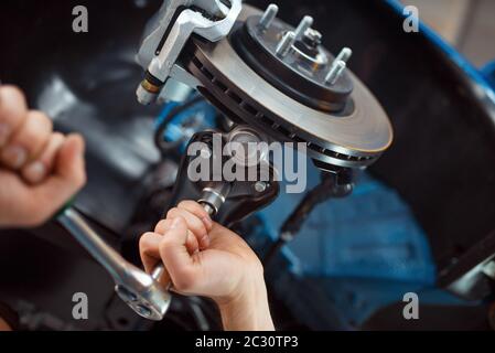Worker in uniform repairing vehicle on lift, car service station. Automobile checking and inspection. Stock Photo
