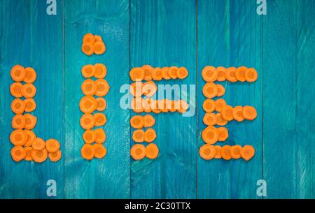 The word life written with carrot slices on blue wooden background. Concept for healthy living and enjoying life Stock Photo