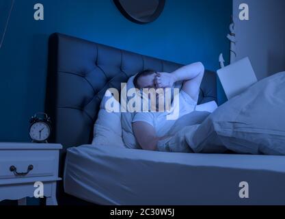 an overtired man works at late night on his laptop Stock Photo