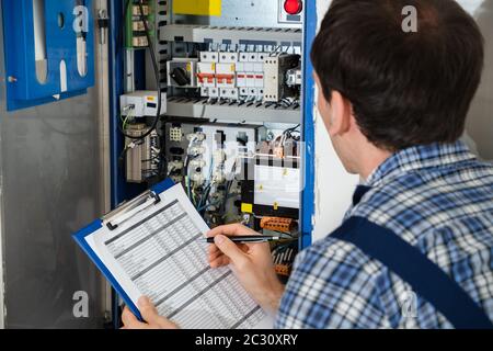 Cropped Image Of Male Electrician Holding Clipboard While Examining Fusebox Stock Photo