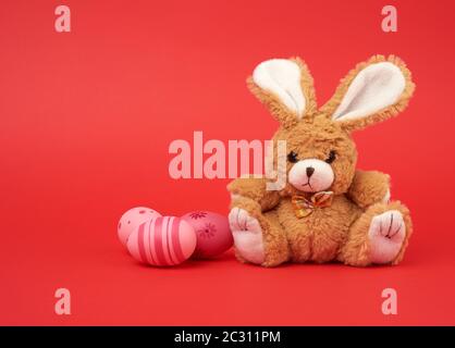 cute brown bunny and pink colored eggs on a red background, easter backdrop Stock Photo