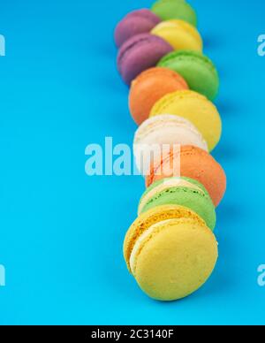 round multi-colored baked macarons with cream lie in a line on a blue background, close up Stock Photo