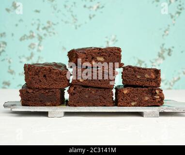 stack of square baked pieces of brownie chocolate cake with walnuts on a wooden board, green background Stock Photo