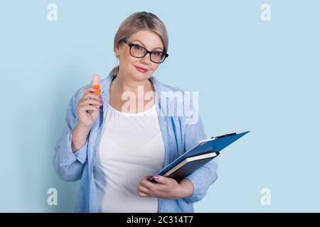 Aged businesswoman with glasses posing on a blue wall with some folders looking at camera and smile Stock Photo