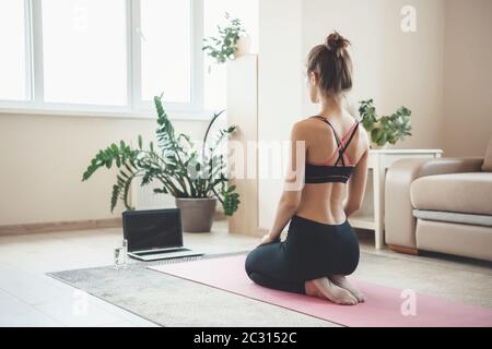 Back view photo of a caucasian sporty woman in sportswear meditating in front of laptop on the floor Stock Photo