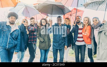 Friends making the best of rain and bad weather standing under umbrellas Stock Photo