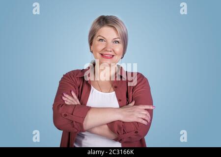Charming senior woman with crossed hands smiling at camera on a blue studio wall Stock Photo