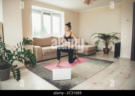 Sporty caucasian woman having online fitness lessons using a laptop and wearing sportswear on floor at home Stock Photo
