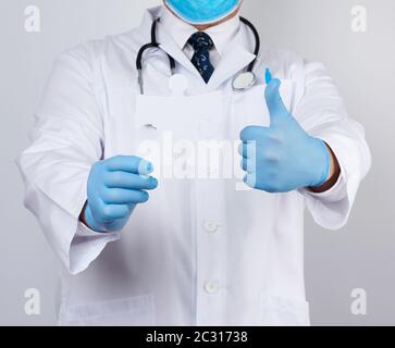 doctor in a white medical coat and blue rubber gloves holds a white paper puzzle, close up