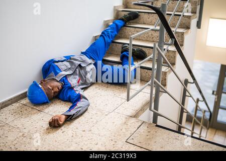 Unconscious Handyman Lying On Staircase With Helmet On Floor Stock Photo