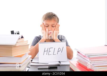 Tired frustrated boy sitting at the table, doing his homework among pile of books. Word Help is written on open notebook Stock Photo