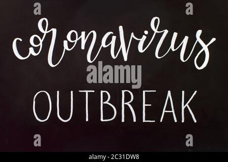 Chalk inscription CORONAVIRUS OUTBREAK on a black chalkboard. Handwritten lettering Stock Photo