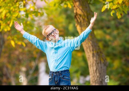 Hilarious seven-year-old boy gleefully raised his hands up in autumn city park Stock Photo