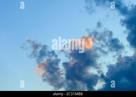 Golden blue evening cloud on a blue sky background. Cloud is partially colored with golden pink by the setting sun.  Beauty in nature. Close-up. Stock Photo
