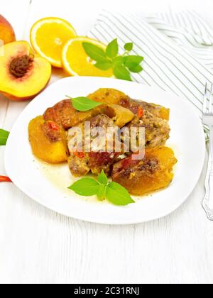 Turkey stewed with peaches, fresh hot pepper and orange sauce, basil leaves in a plate, napkin, fruits on wooden board background Stock Photo