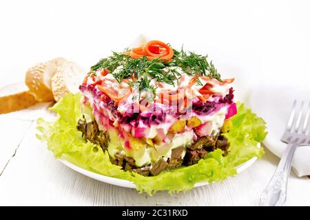 Puff salad with beef, boiled potatoes and beets, pears, spicy Korean carrots, seasoned with mayonnaise and garnished with dill on a green lettuce in a Stock Photo