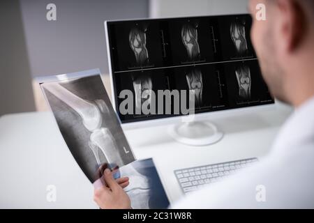 Mature Male Doctor Examining Knee X-ray In Clinic Stock Photo
