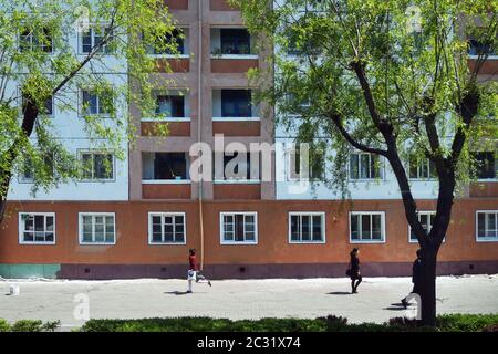 Pyongyang, North Korea - May 2, 2019: People go down on the street in suburb of city, typical apartments house in background Stock Photo