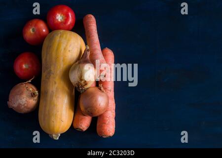 Some onions, tomatoes, carrots and a butternut squash on a blue background Stock Photo