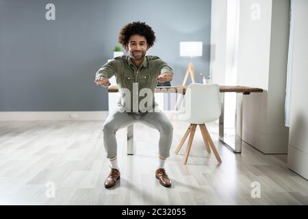 Smiling Young Businessman Doing Sit-ups At Workplace Stock Photo