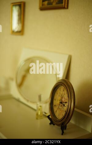 Antique Paris clock on a white vanity table with an oval mirror and paintings on the wall. Stock Photo